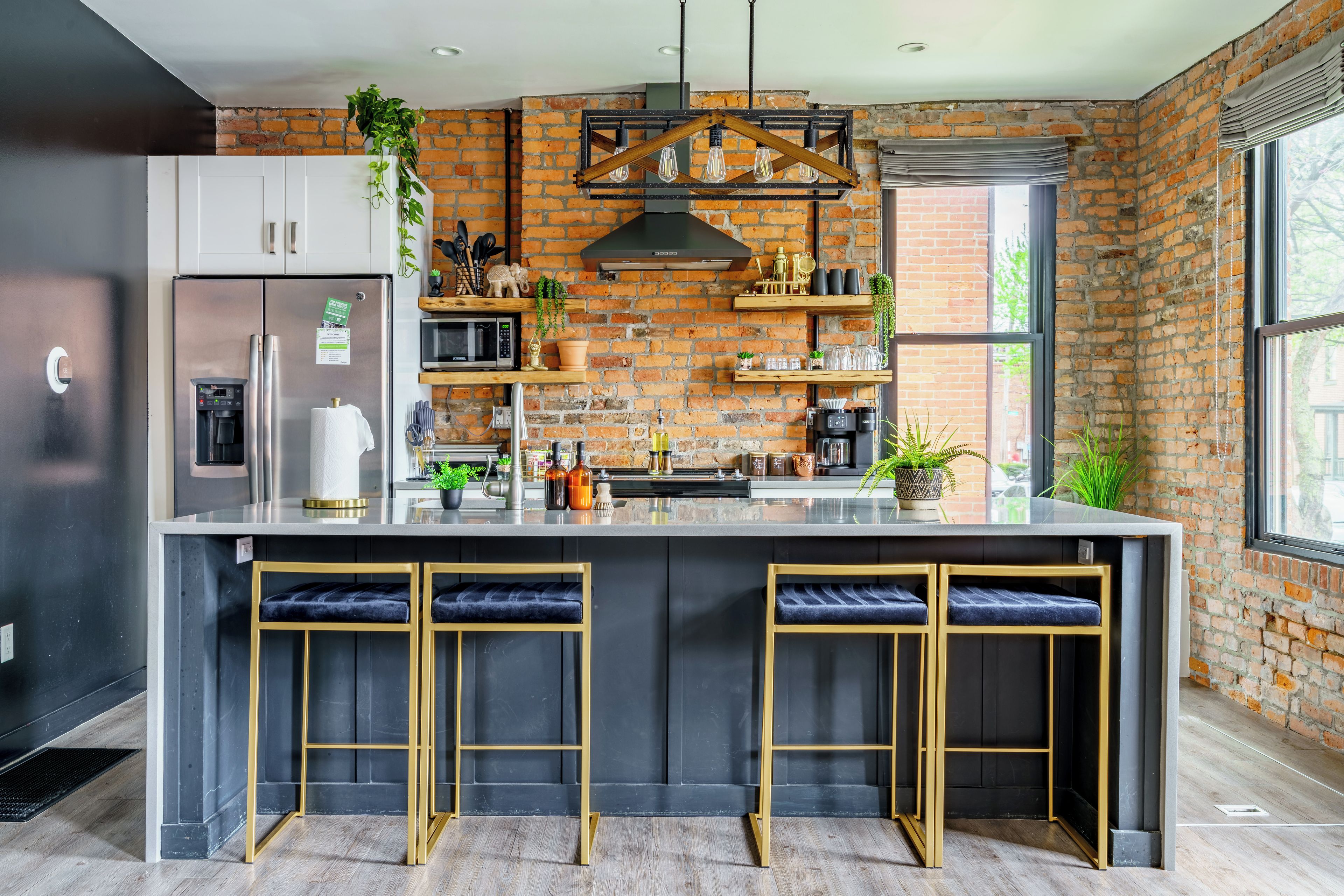 A modern kitchen with a central island, bar stools, a refrigerator, and a brick wall.