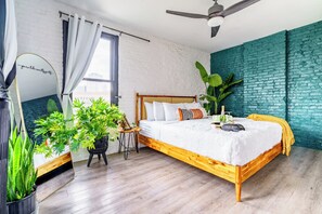 A modern bedroom with a wooden bed, a ceiling fan, and a large window. - Jungle House Downtown Columbus – Modern Boutique Suites (Columbus)