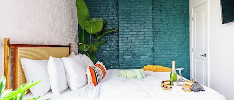 A bedroom with a white brick wall, a wooden headboard, and a bed with white bedding.