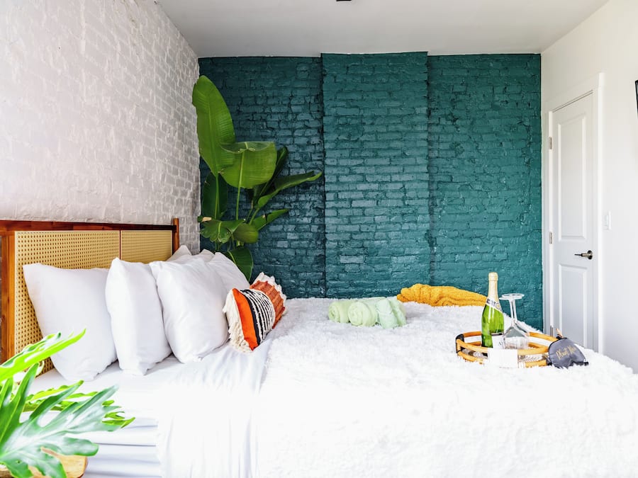 A bedroom with a white brick wall, a wooden headboard, and a bed with white bedding.