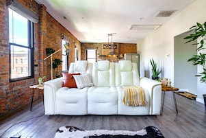 A modern living room with a white leather sofa, a brick wall, and a large window.