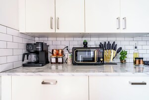 Una cocina moderna con armarios blancos, cafetera, microondas, tostadora y diversos utensilios de cocina.