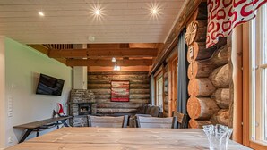 Interior rústico de cabana com lareira de pedra, paredes de madeira e uma mesa de jantar.