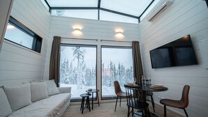Une pièce confortable avec un canapé, une table à manger, des chaises et un téléviseur. De grandes fenêtres offrent une vue sur le paysage enneigé.