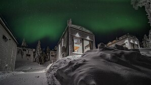 Un paysage enneigé avec une maison illuminée par la lumière provenant de l’intérieur, entourée d’arbres couverts de neige et d’une pile de neige.