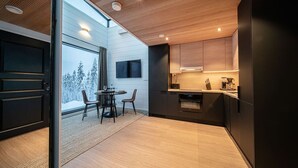 Une cuisine moderne avec des meubles en bois, un coin repas comprenant une table et des chaises, et une grande fenêtre offrant une vue sur des arbres couverts de neige.