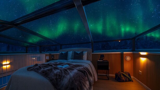 Une chambre avec un lit, une table de chevet, une chaise et une fenêtre donnant sur les aurores boréales.