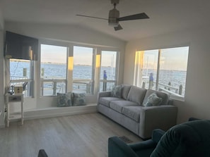 A living room with a sofa, a TV, and large windows overlooking a body of water.