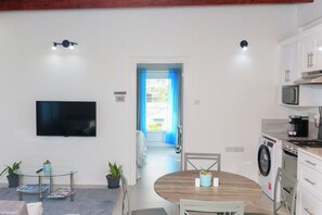 A modern kitchen with a microwave, stove, and washing machine. There is a dining area with a round table and chairs, and a TV mounted on the wall. - Agape Suites (Soufrière)