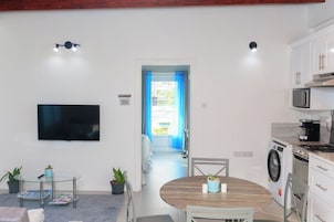 Cocina moderna equipada con microondas, estufa y lavadora. Hay un comedor con una mesa redonda y sillas, y un televisor montado en la pared.