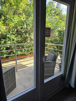 A room with a sliding glass door leading to a balcony with a metal railing and wicker furniture. - Agape Suites (Soufrière)