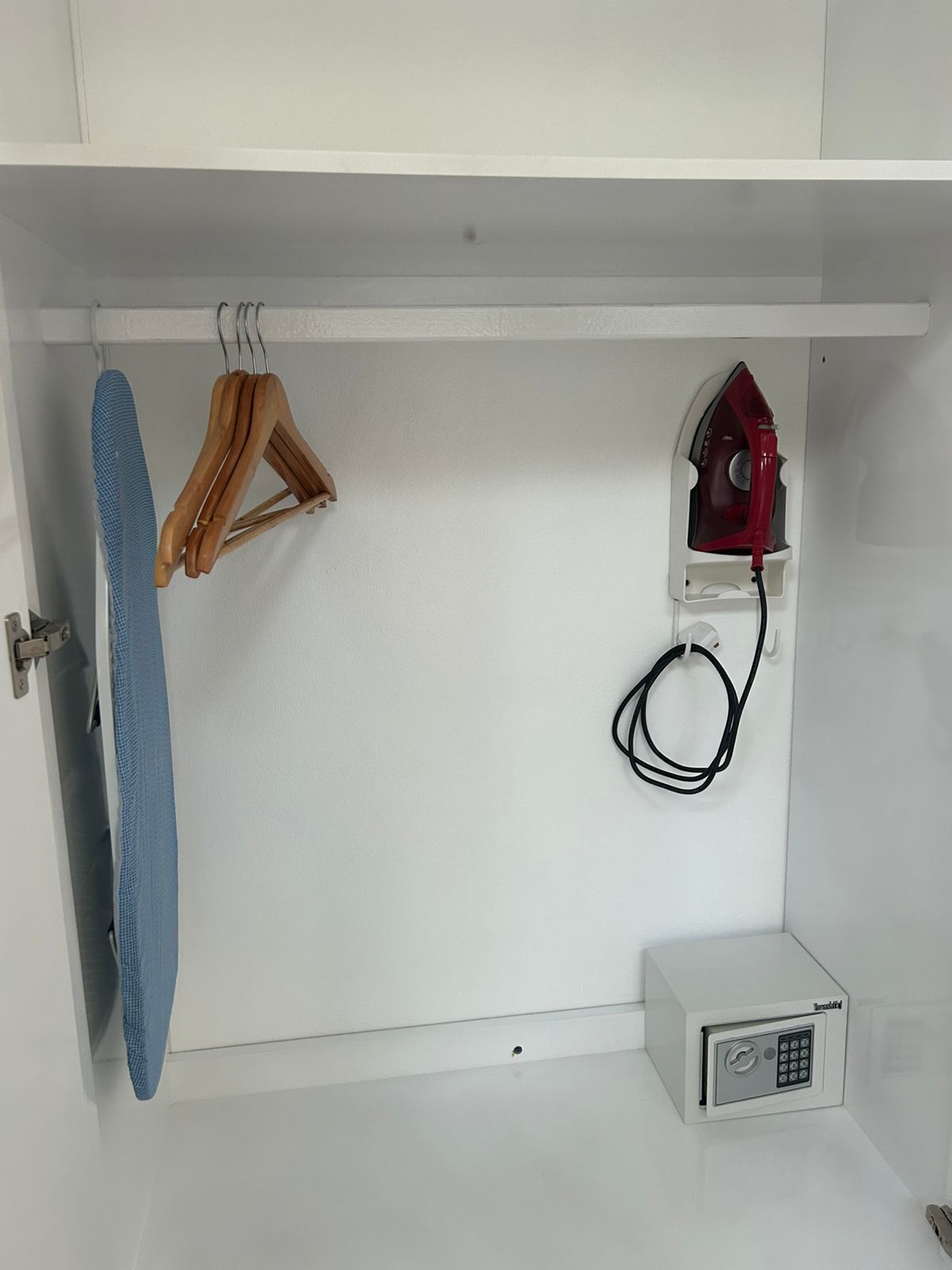 A white cabinet with a hanging rack, an iron, and a small appliance.