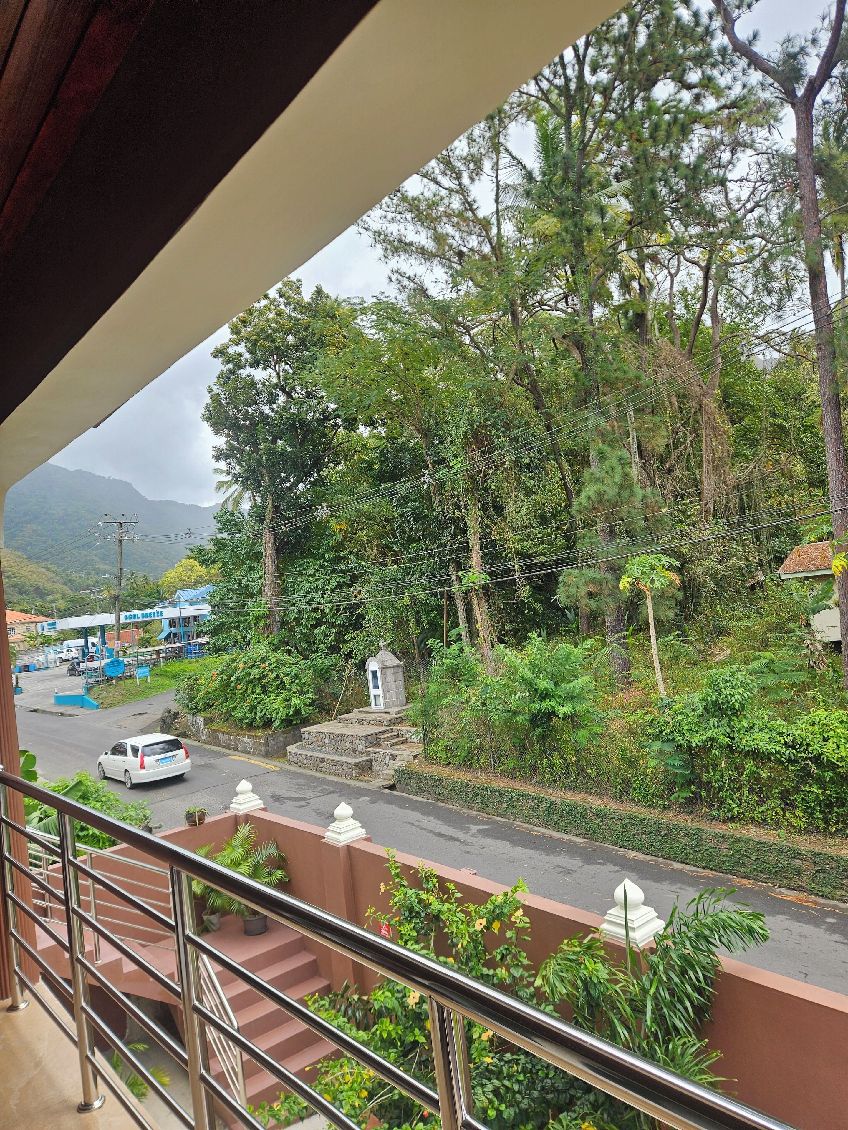 A view from a balcony overlooking a road with a gas station and a small shrine.