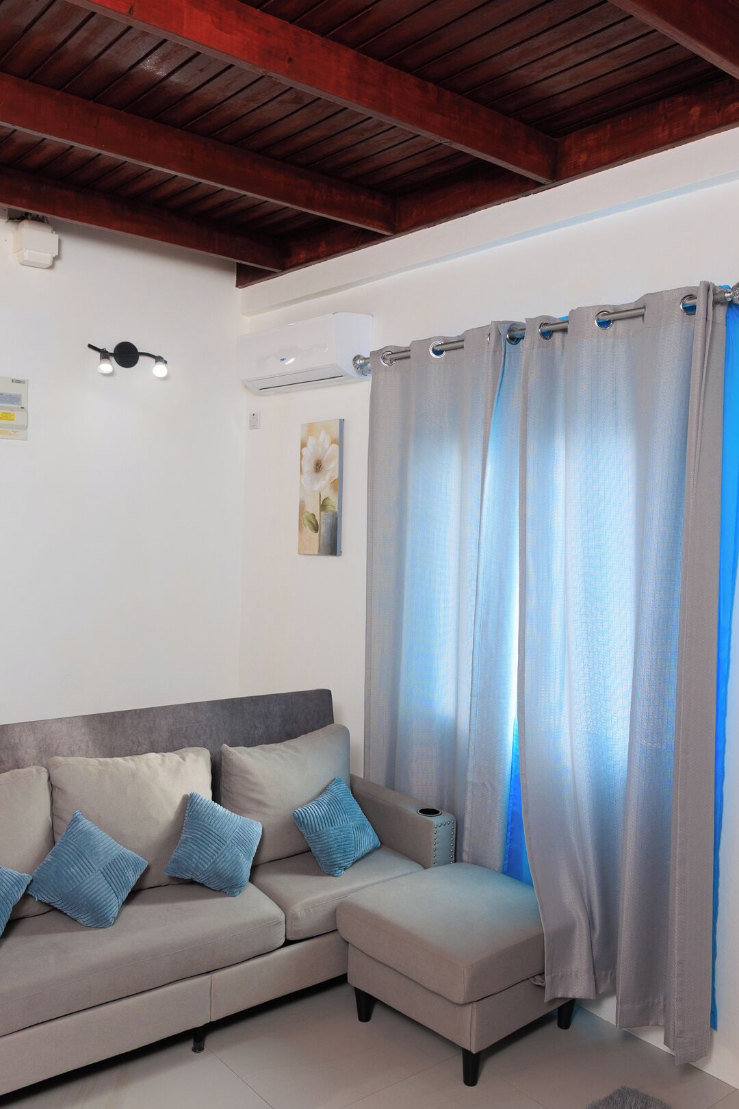 Una sala de estar con sofá, una mesita, un ventilador de techo y una ventana con cortinas.