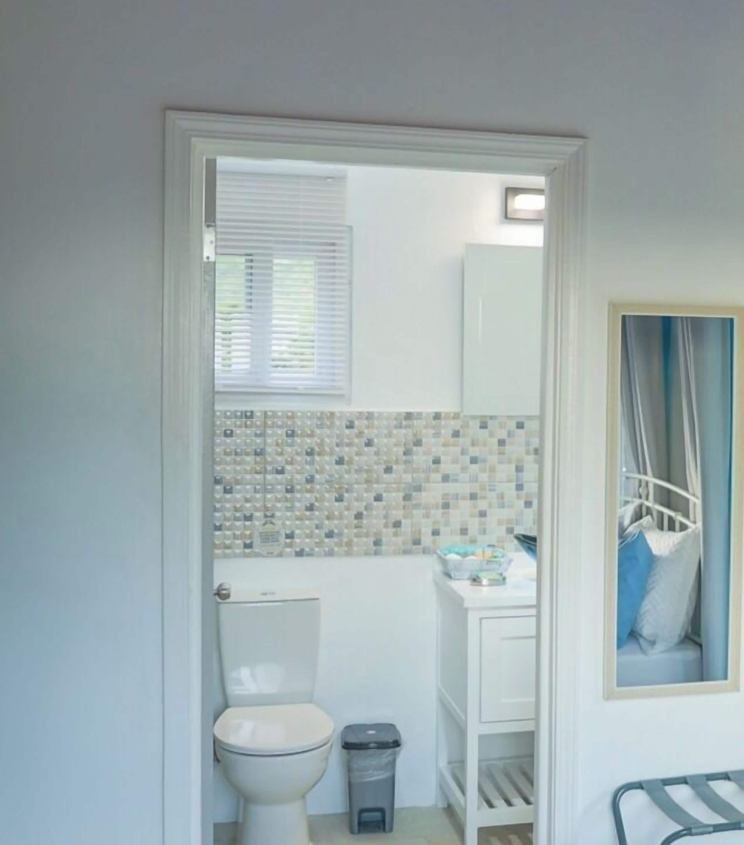 A bathroom with a toilet, a trash bin, a sink, and a tiled backsplash.