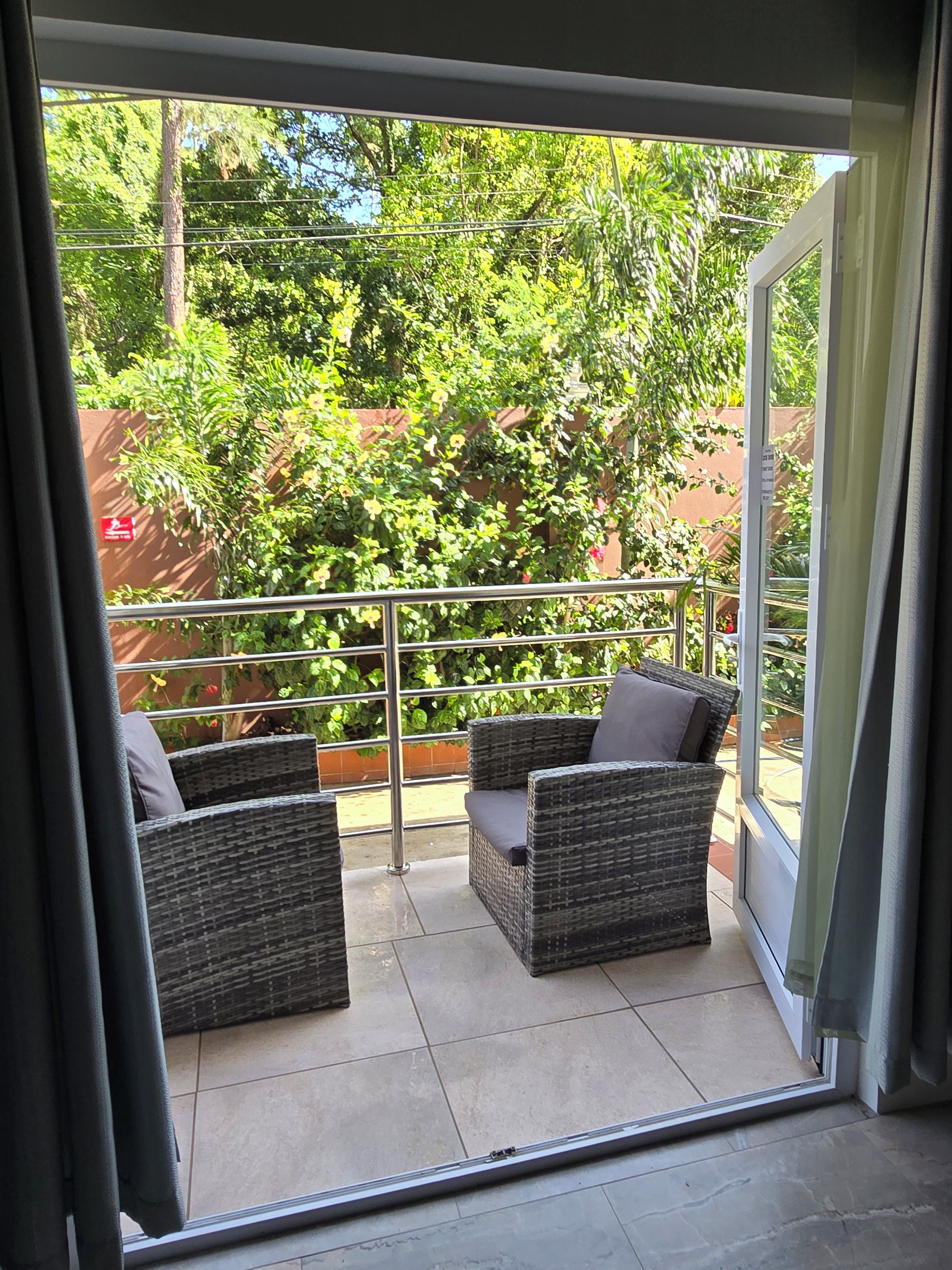 A balcony with wicker furniture and a glass door leading to a garden.