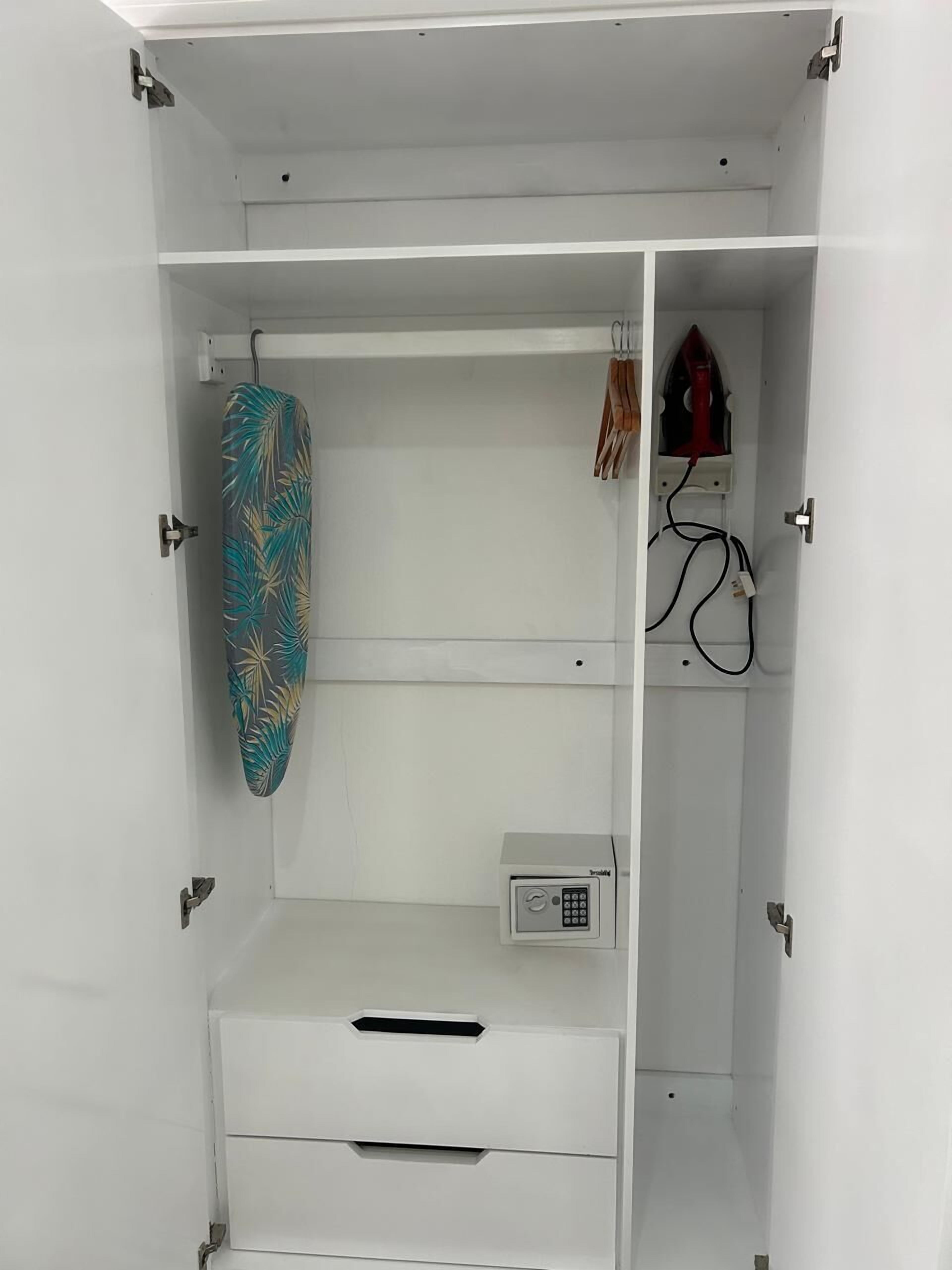 Une armoire blanche dotée d’une planche à repasser intégrée, d’une petite prise électrique et d’une tringle pour suspendre les vêtements.