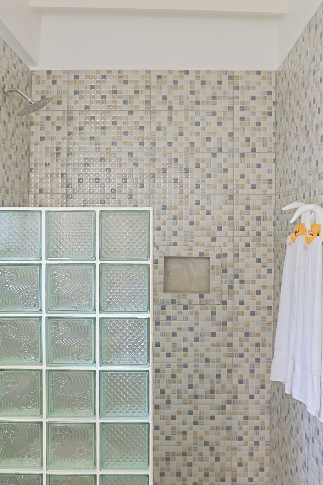 Un baño con paredes de mosaicos, cabina de ducha de vidrio y toallero con toallas blancas.