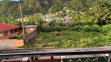 Un balcón con vistas a un pueblo en la ladera, un edificio de techo rojo y un césped verde con una guirnalda decorativa.