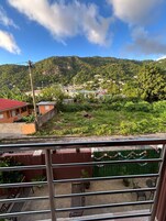 Un balcón con vistas a un pueblo en la ladera, un edificio de techo rojo y un césped verde con una guirnalda decorativa.