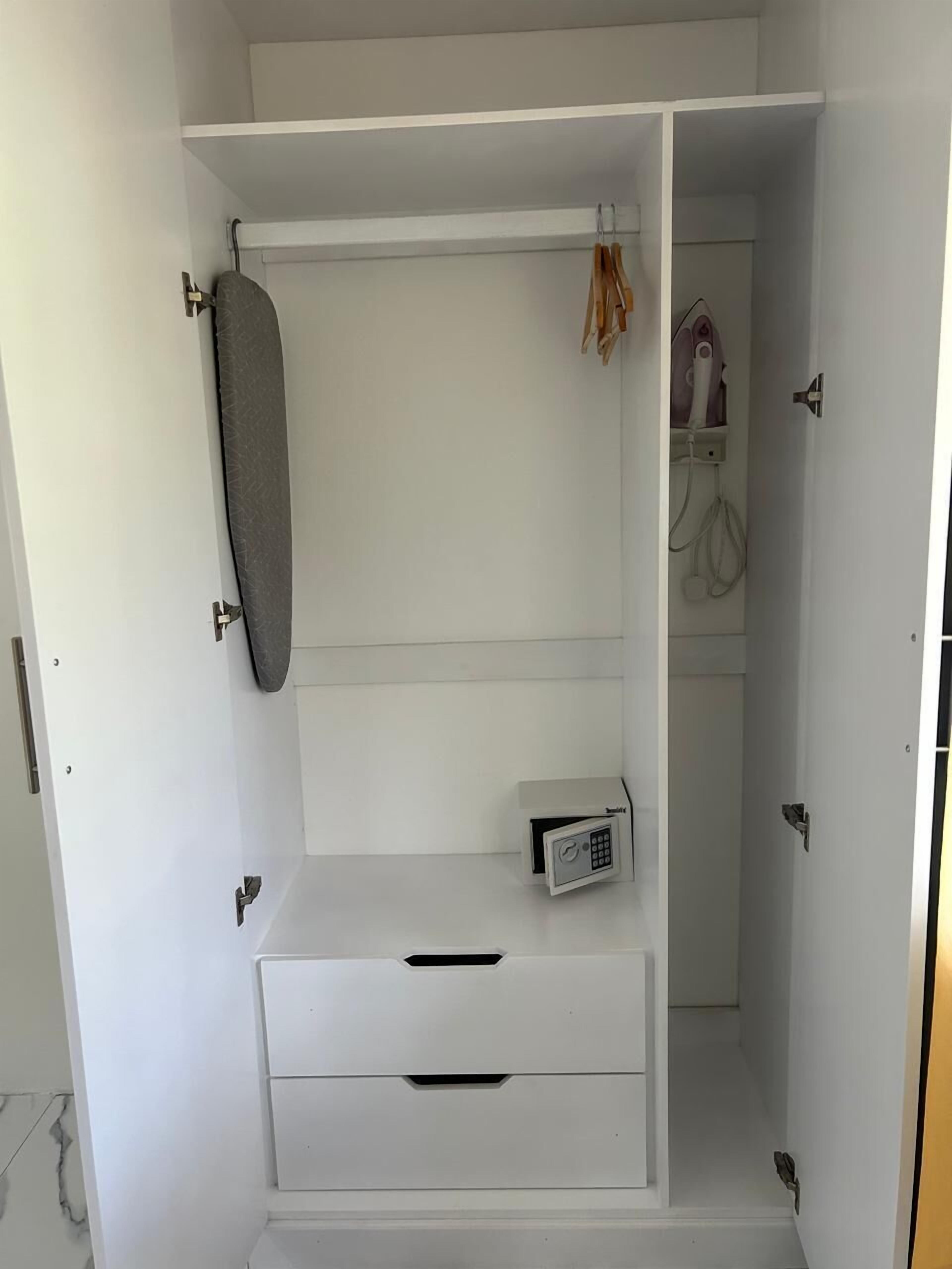 A white wardrobe with a hanging iron, a small safe, and a towel rack.