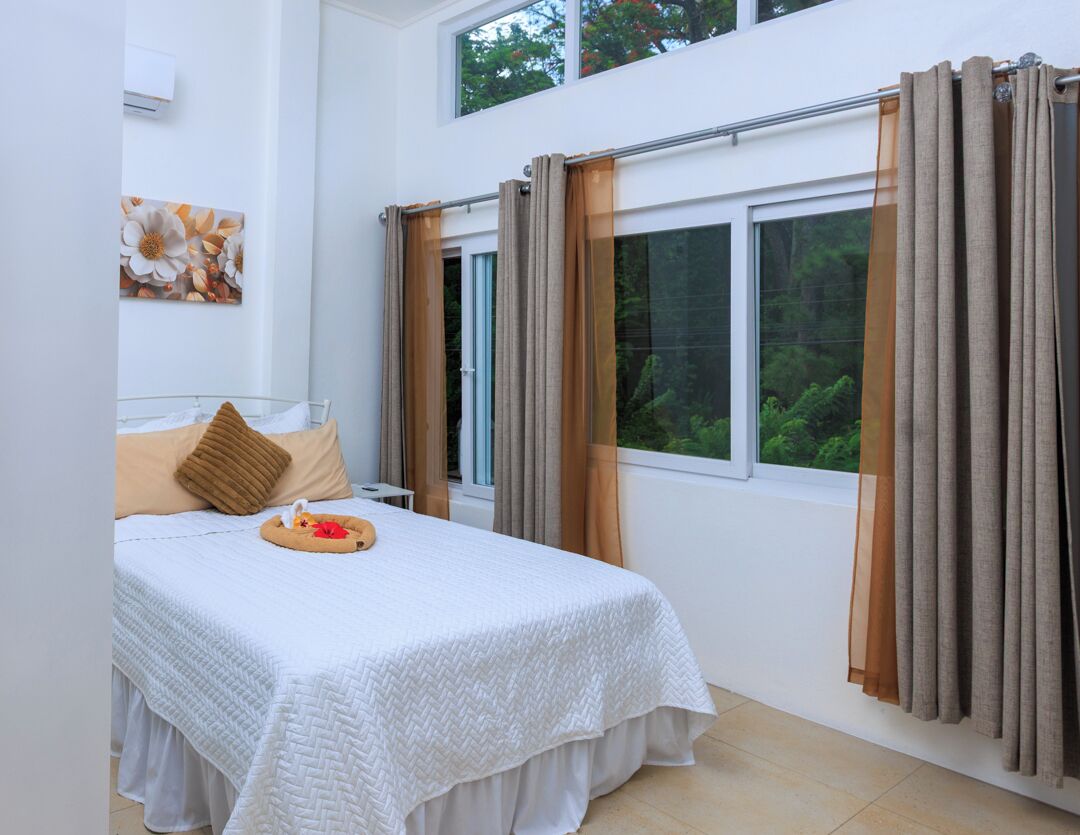 A bedroom with a bed, curtains, a window, and a wall-mounted air conditioner.