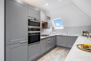 A modern kitchen with grey cabinets, a built-in oven, and a skylight.