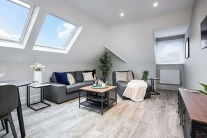 A modern living room with a grey sofa, a coffee table, a dining table, and a plant.