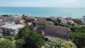 A coastal residential area with various buildings, including a prominent house with a steep roof and a smaller building with a flat roof.