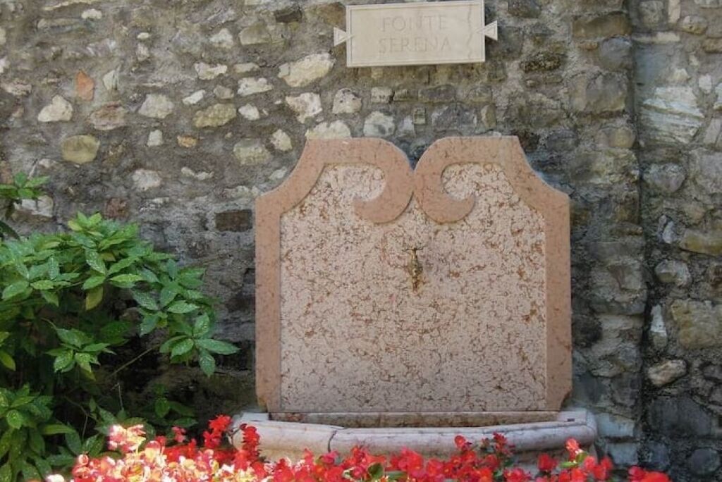 Ein steinernes Grabmal mit einem Schild darüber, vor einer Steinmauer.
