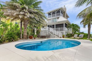 Une maison à deux étages avec une piscine, entourée de palmiers et dotée d’un patio.