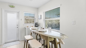 Una cocina con una puerta blanca, una cafetera y una ventana con persianas.