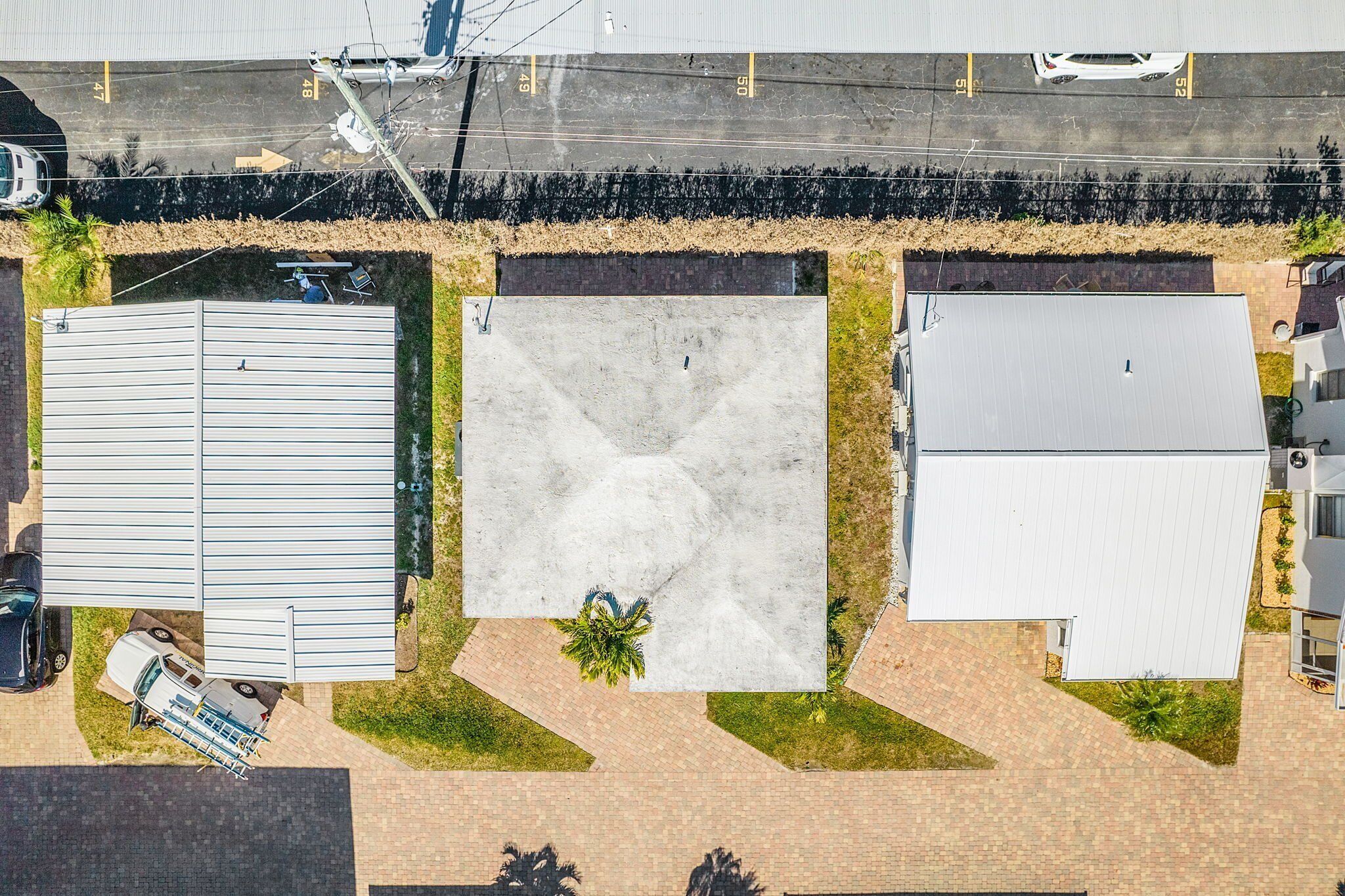 Une vue aérienne d’un parking où se trouvent plusieurs véhicules, d’un grand bâtiment doté d’un toit plat et d’une construction plus petite avec un toit en pente.
