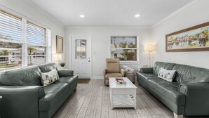 A living room with two green leather sofas, a white coffee table, and a beige armchair. - A Great Day At The Beach! - Aloha Kai #6 - Roelens (Sarasota)