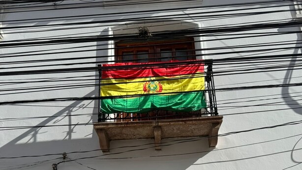 A building with a wooden door and a balcony with a flag. - Krass casa de huespedes (Sucre)