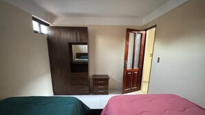 A bedroom with two beds, a wardrobe, a small table, and a mirror. - Krass casa de huespedes (Sucre)