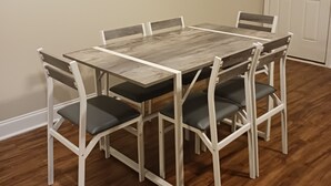 Un coin repas avec une table en bois et six chaises, une porte blanche et deux éléments de décoration murale.