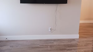 Une pièce avec un téléviseur à écran plat fixé au mur, une plinthe blanche et un plancher en bois.