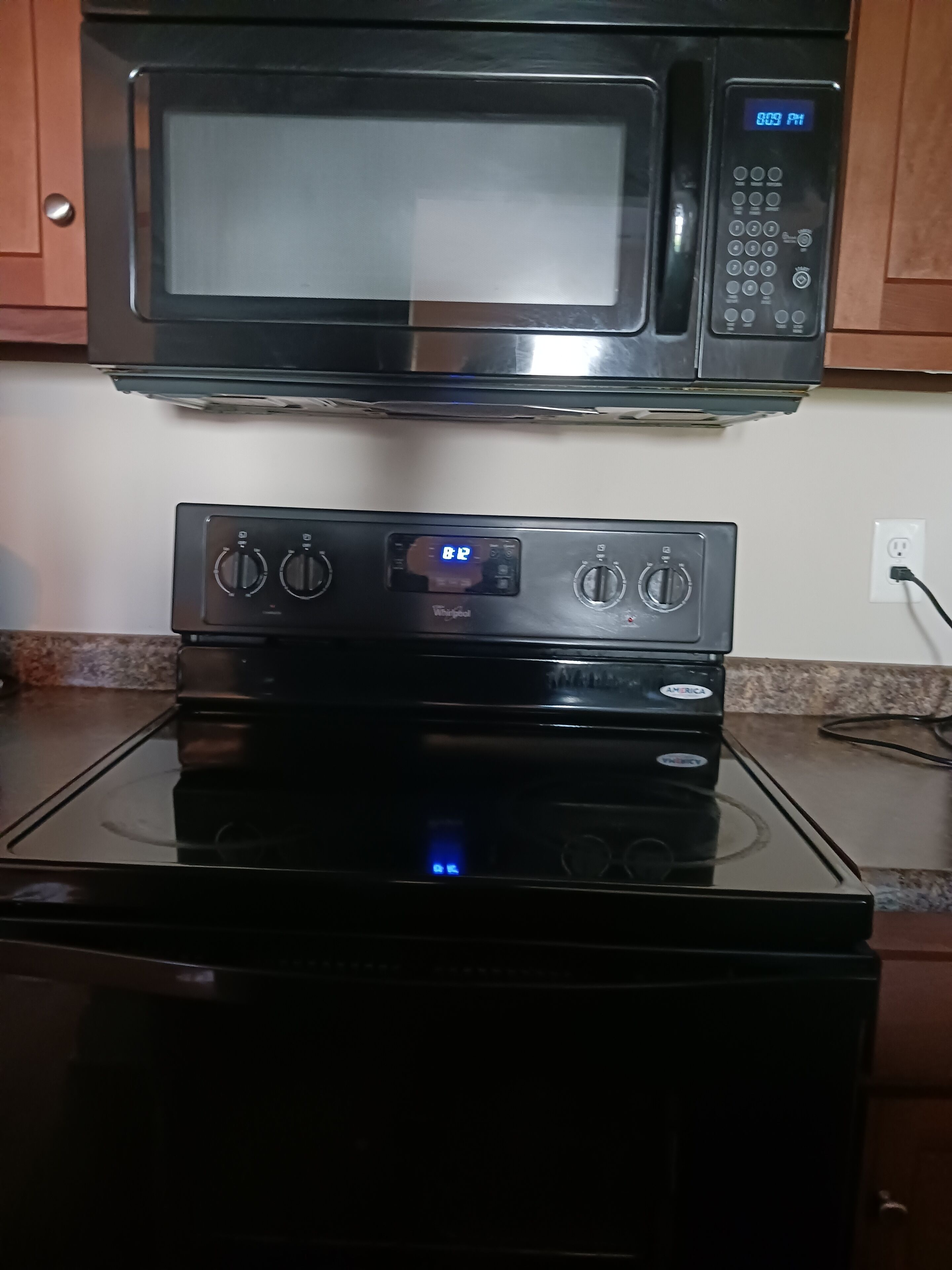 A kitchen with a microwave above a stove, a digital clock, and a power outlet on the countertop.
