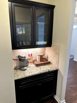 A kitchen with dark cabinets, a coffee maker, and a countertop with various items. - Spacious LUXE Home | RTP/Airport (Durham)