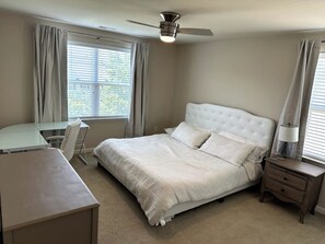 A bedroom with a bed, a desk, a chair, a nightstand, and a ceiling fan.
