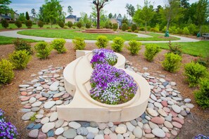 A landscaped garden with a winding path, a circular flower bed with purple flowers, and a central tree.