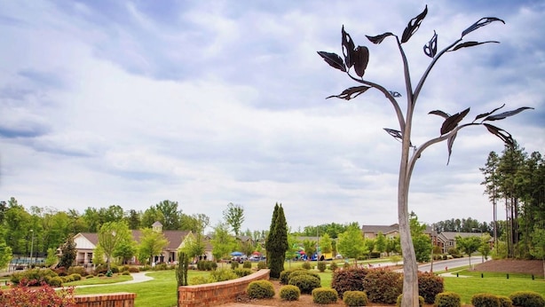 A landscaped area with a central sculpture, paved walkways, and residential buildings in the background. - Spacious LUXE Home in RTP / near Airport (Durham)