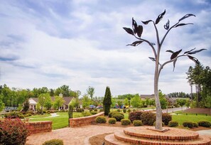A landscaped area with a central sculpture, paved walkways, and residential buildings in the background. - Spacious LUXE Home in RTP / near Airport (Durham)