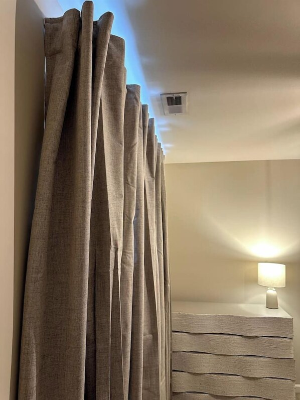 A room with a curtain, a wall-mounted light, and a textured wall.