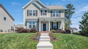 A two-story house with a front porch, a small front yard, and a clear sky. - Spacious LUXE Home in RTP / near Airport (Durham)