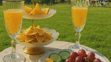 Una mesa con dos vasos de jugo de naranja, un bol de papas fritas y un plato con uvas y rodajas de pepino.