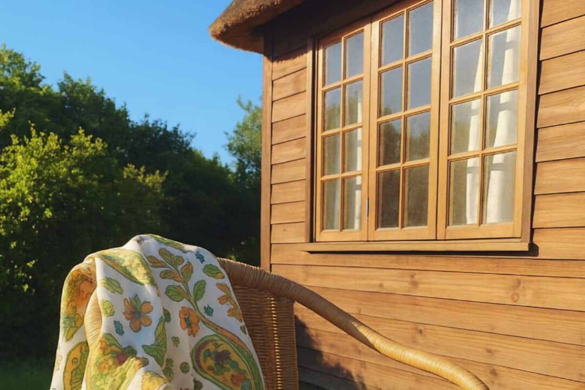 A wooden building with large windows and a wicker chair with a floral blanket.