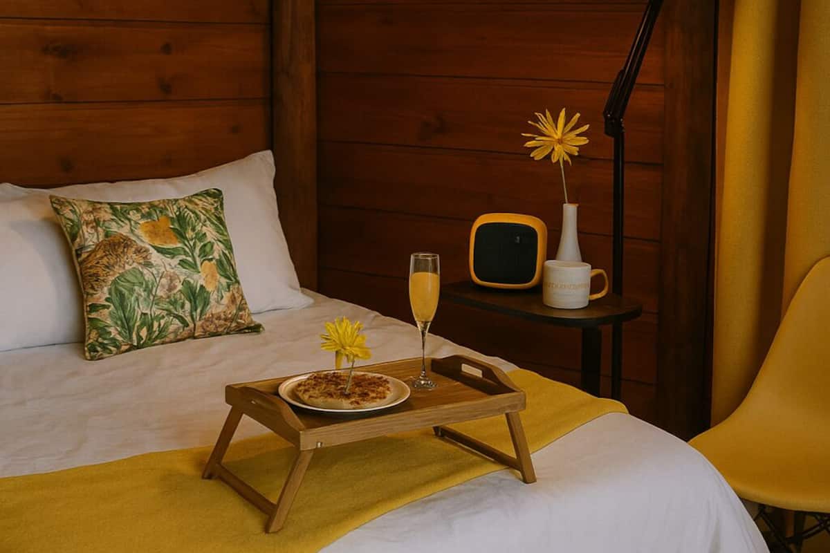 A cozy room with a bed, a bedside table with a lamp, a chair, and a tray with breakfast items.
