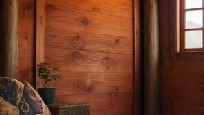 A wooden room with a bed, a pillow, a potted plant, and a window. - African Hut  (Tulbaghweg)